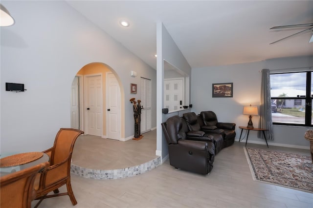 living area featuring light wood finished floors, arched walkways, baseboards, lofted ceiling, and ceiling fan