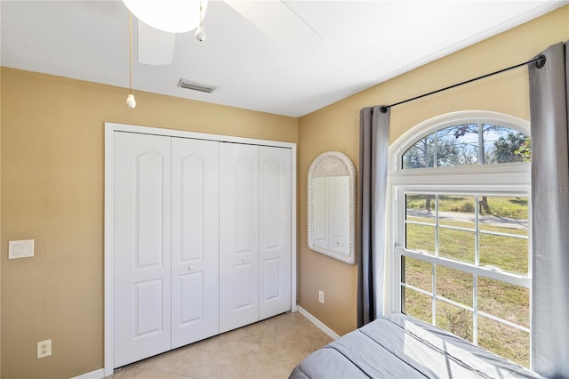 bedroom with ceiling fan, light tile patterned flooring, visible vents, baseboards, and a closet