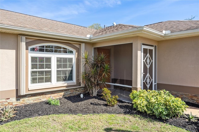 entrance to property featuring roof with shingles and stucco siding