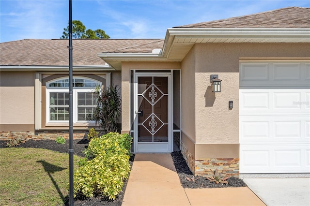 view of exterior entry with an attached garage, stone siding, a shingled roof, and stucco siding