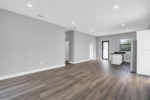 unfurnished living room with dark wood finished floors, recessed lighting, baseboards, and a sink