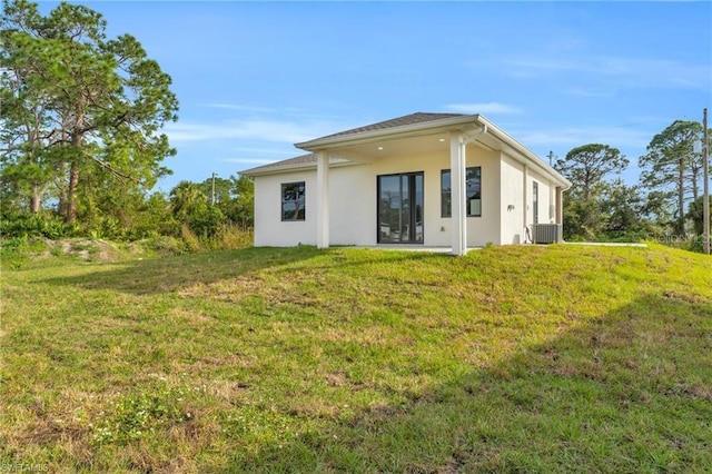 rear view of house featuring central air condition unit, stucco siding, and a yard