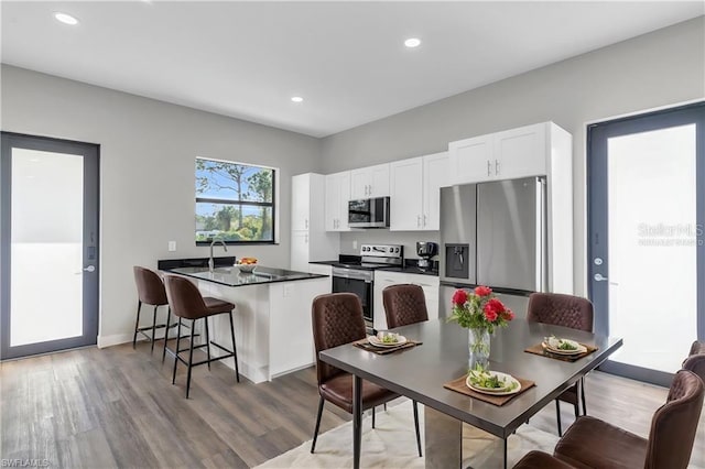 kitchen featuring dark countertops, a peninsula, stainless steel appliances, light wood-style floors, and white cabinetry