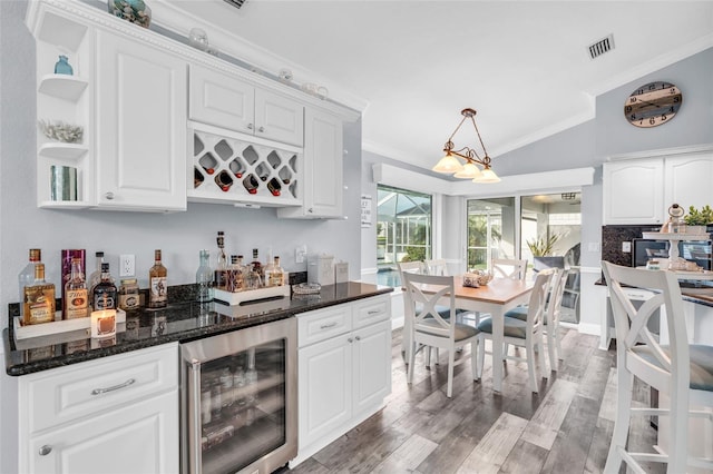 bar with beverage cooler, light wood-type flooring, vaulted ceiling, crown molding, and a bar