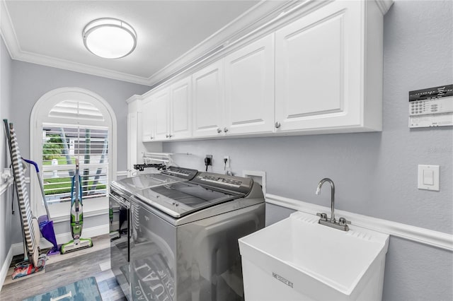 laundry room featuring cabinet space, wood finished floors, crown molding, washer and dryer, and a sink