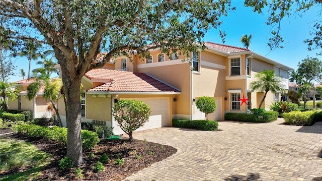 mediterranean / spanish-style house with a garage, decorative driveway, a tile roof, and stucco siding