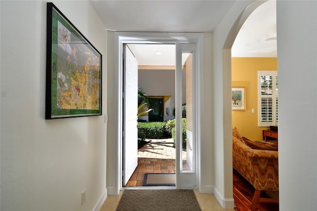 doorway with arched walkways, tile patterned floors, a wealth of natural light, and baseboards