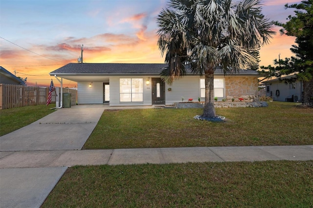 view of front of property featuring an attached carport, fence, driveway, stone siding, and a front yard