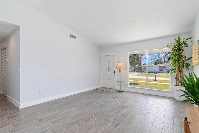 empty room featuring visible vents, vaulted ceiling, baseboards, and wood finished floors