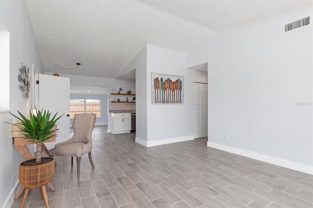 sitting room featuring baseboards, visible vents, vaulted ceiling, a bar, and light wood-style floors