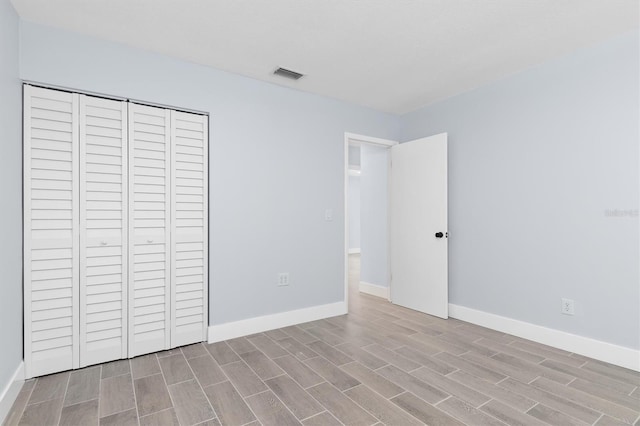 unfurnished bedroom featuring wood tiled floor, a closet, visible vents, and baseboards