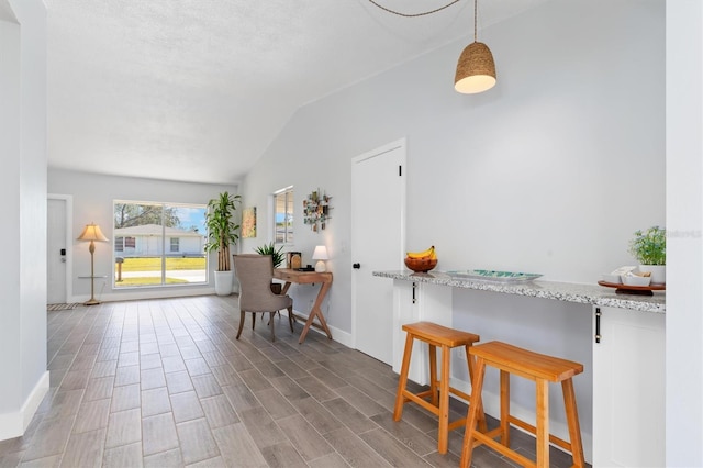 kitchen with light stone counters, baseboards, vaulted ceiling, hanging light fixtures, and wood tiled floor