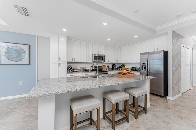 kitchen with a breakfast bar area, stainless steel appliances, visible vents, white cabinets, and a sink