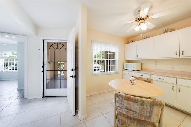 kitchen featuring light tile patterned floors, baseboards, a ceiling fan, white microwave, and light countertops