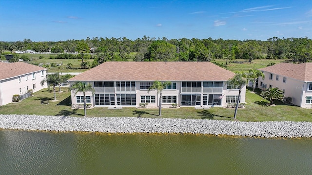 rear view of house featuring a water view, a sunroom, and a lawn