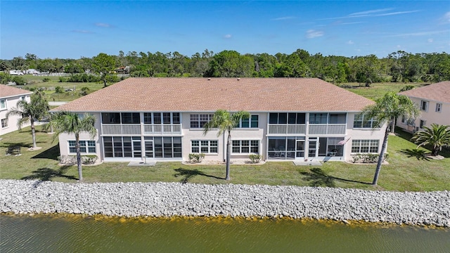 back of property with a sunroom, a water view, and a yard