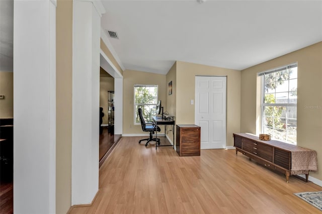 home office featuring light wood-style floors, baseboards, visible vents, and vaulted ceiling