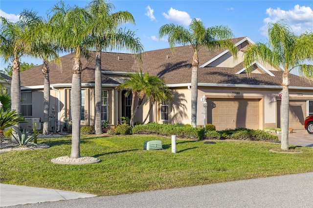 view of front of house featuring an attached garage, driveway, roof with shingles, stucco siding, and a front yard