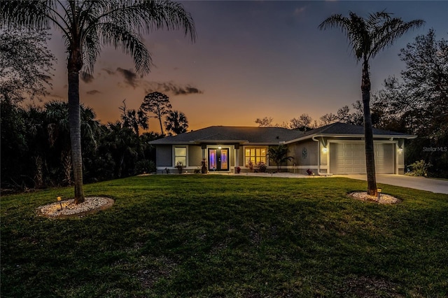 view of front facade featuring an attached garage, concrete driveway, a lawn, and french doors