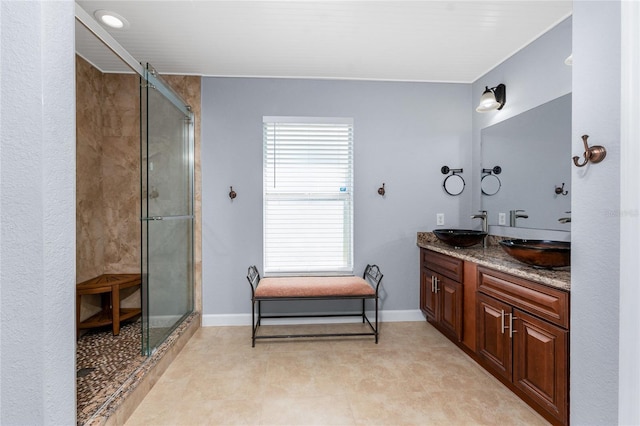 bathroom with a stall shower, a sink, baseboards, and double vanity