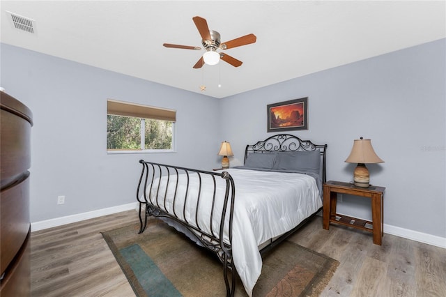 bedroom featuring a ceiling fan, visible vents, baseboards, and wood finished floors