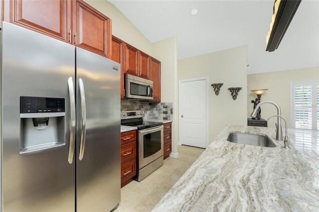 kitchen with reddish brown cabinets, decorative backsplash, appliances with stainless steel finishes, light stone countertops, and a sink