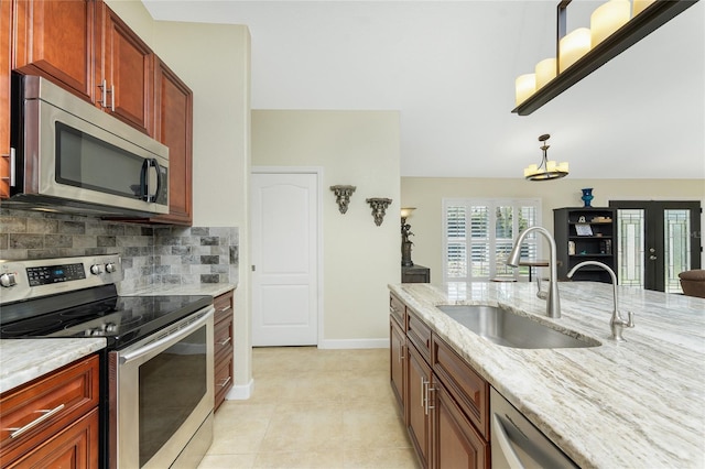 kitchen featuring french doors, tasteful backsplash, appliances with stainless steel finishes, a sink, and light stone countertops