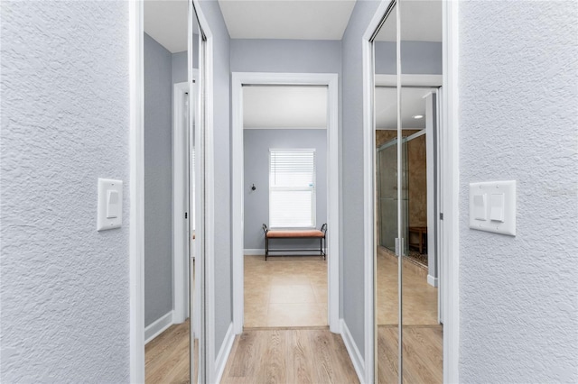 hall with light wood-style floors, baseboards, and a textured wall