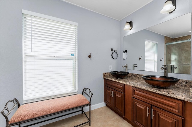 bathroom with double vanity, a shower stall, baseboards, and a sink