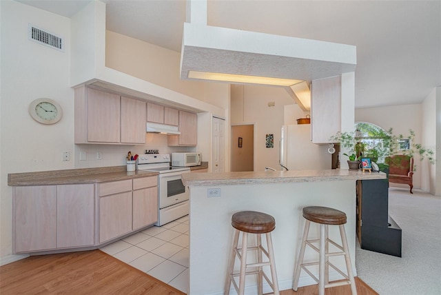 kitchen featuring visible vents, light brown cabinetry, a peninsula, white appliances, and under cabinet range hood