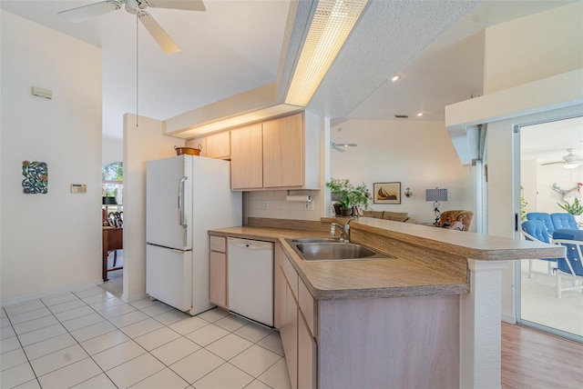 kitchen featuring white appliances, open floor plan, a peninsula, light brown cabinets, and a sink