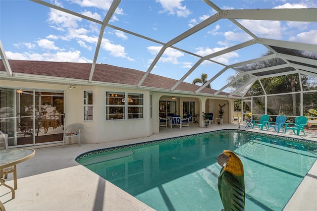 outdoor pool featuring glass enclosure, ceiling fan, and a patio