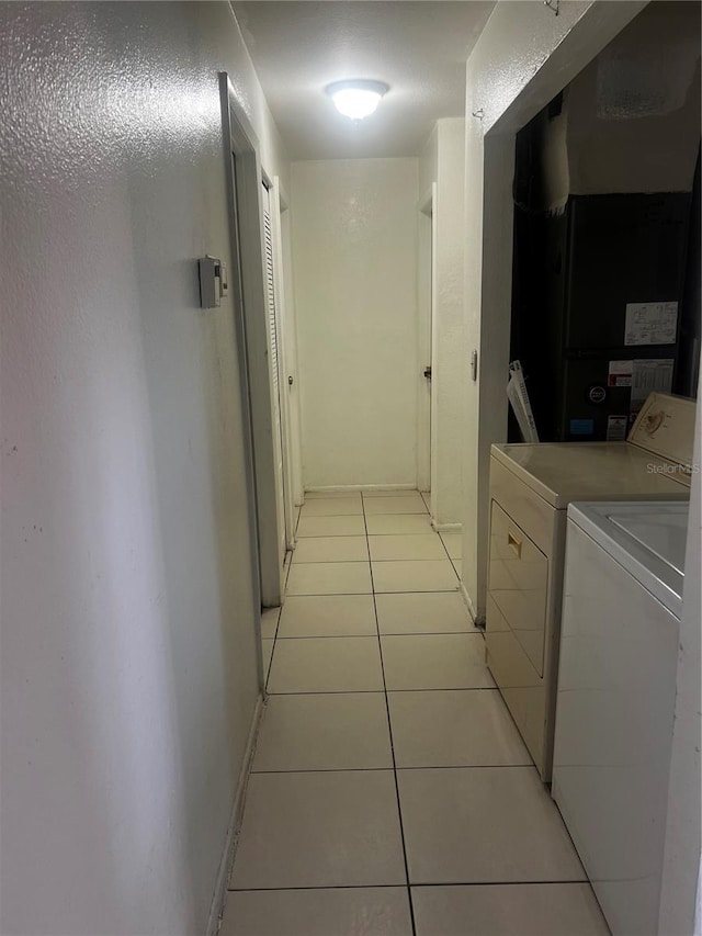 hall featuring independent washer and dryer, baseboards, and light tile patterned floors