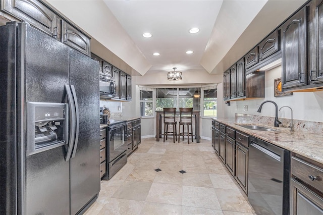 kitchen featuring black appliances, light stone counters, dark brown cabinets, and a sink