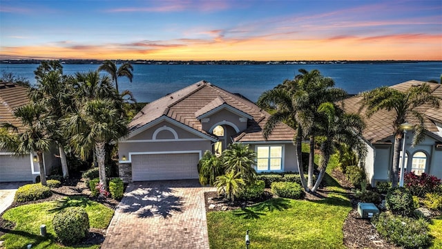 view of front of property with an attached garage, a water view, decorative driveway, and stucco siding