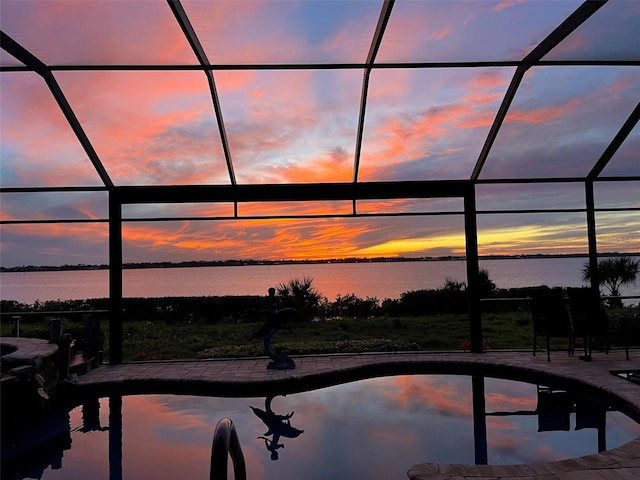 pool at dusk with glass enclosure, a water view, and a patio