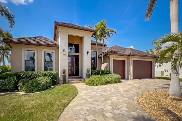 prairie-style home featuring a tiled roof, decorative driveway, an attached garage, and stucco siding