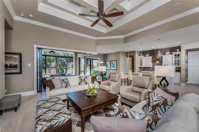 living room with light wood finished floors, baseboards, a raised ceiling, a high ceiling, and crown molding