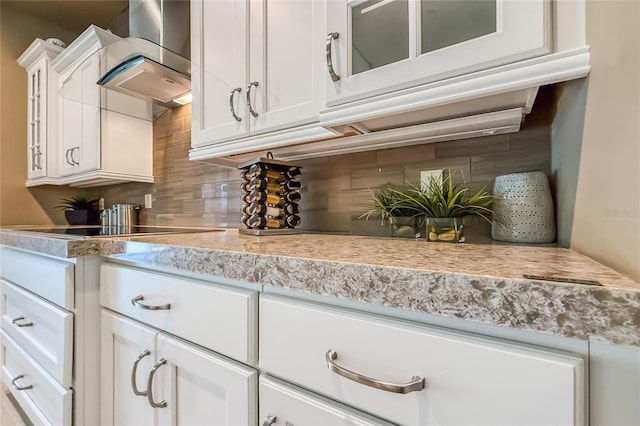 interior space with tasteful backsplash, glass insert cabinets, white cabinets, wall chimney exhaust hood, and black electric cooktop