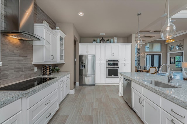 kitchen with decorative backsplash, appliances with stainless steel finishes, white cabinetry, a sink, and wall chimney range hood