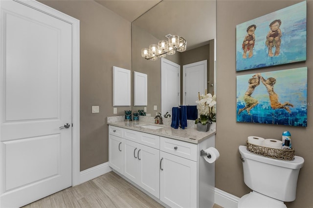 bathroom with toilet, wood finished floors, vanity, baseboards, and an inviting chandelier