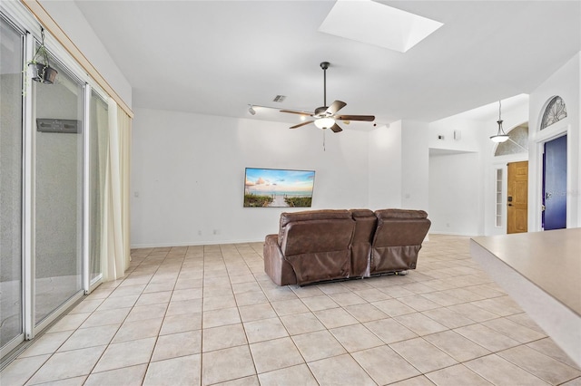 living area featuring visible vents, baseboards, vaulted ceiling with skylight, light tile patterned flooring, and a ceiling fan