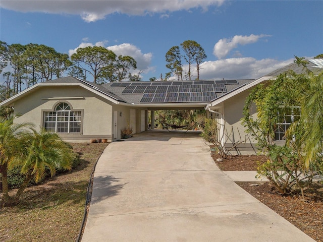 view of front of property featuring stucco siding, a carport, solar panels, and driveway