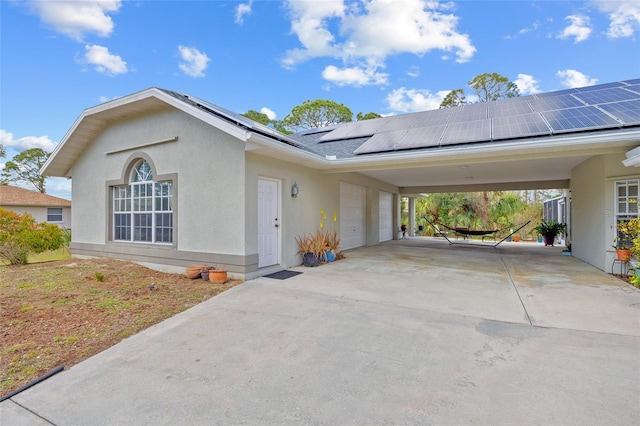 view of side of property with an attached carport, stucco siding, concrete driveway, a garage, and roof mounted solar panels