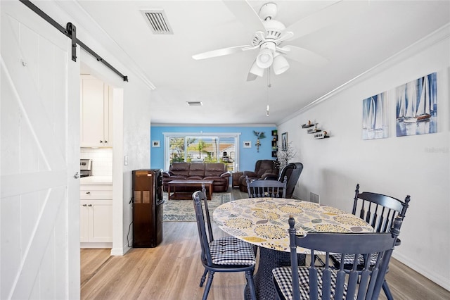 dining space featuring visible vents, crown molding, ceiling fan, a barn door, and light wood-style floors