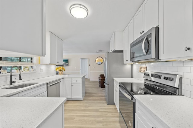 kitchen featuring light wood-type flooring, a sink, a peninsula, appliances with stainless steel finishes, and white cabinets