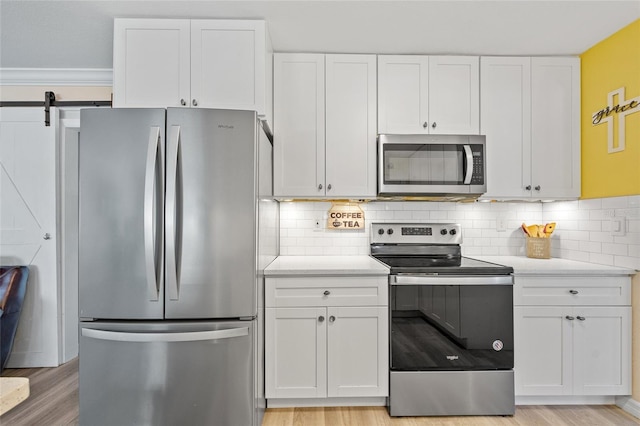 kitchen with light wood finished floors, white cabinets, appliances with stainless steel finishes, and light countertops