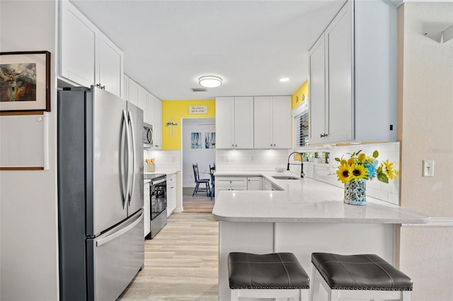 kitchen featuring a sink, white cabinetry, appliances with stainless steel finishes, a peninsula, and light wood finished floors