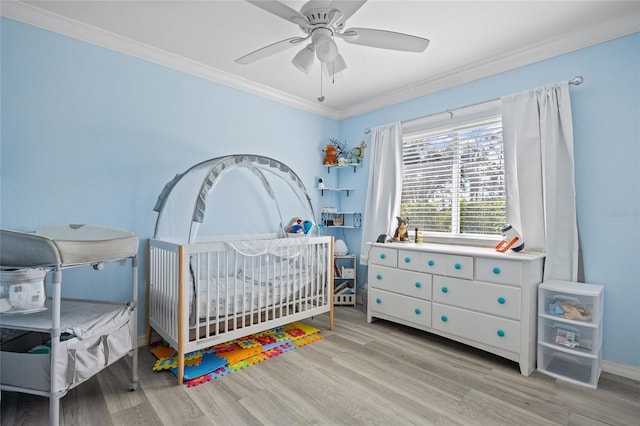 bedroom with crown molding, baseboards, ceiling fan, light wood-type flooring, and a nursery area