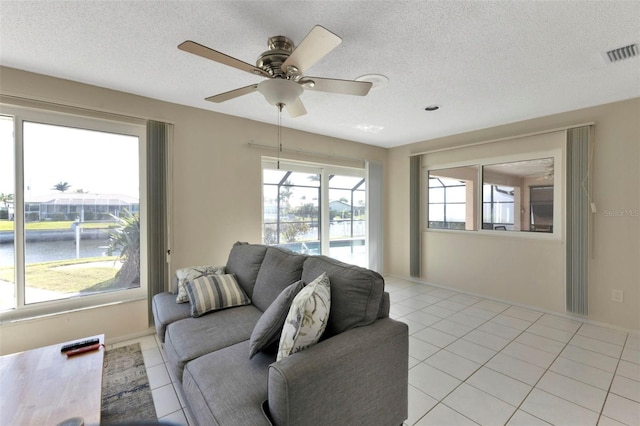 living area with light tile patterned floors, visible vents, a water view, ceiling fan, and a textured ceiling
